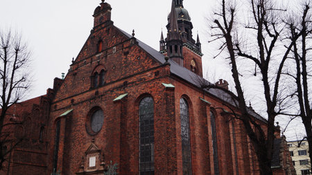 A red brick Church of the Holy Spirit with a spire, framed by trees against an overcast sky. Copenhagen, Denmark.の写真素材