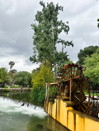 A wooden watermill wheel situated by a riverbank surrounded by lush greenery and trees.の写真素材