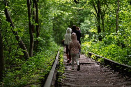 Kids strolling on a quiet railway path encompassed by tall green treesの写真素材