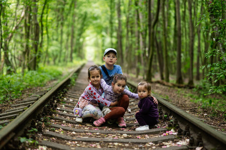 Group of children sitting on disused railway tracks surrounded by dense green forest.の写真素材