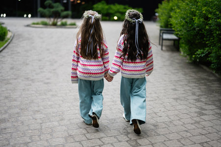 Two twin girls in colorful sweaters walking hand in hand down a cobblestone pathの写真素材