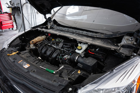 A car engine exposed under its raised hood inside a maintenance and repair shop