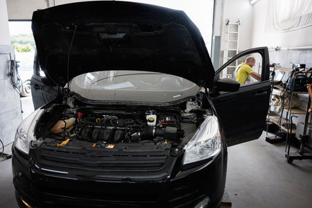 Open car hood in an active workshop with mechanic performing diagnostics and maintenance