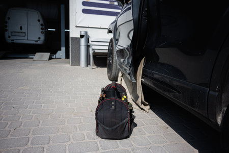 A toolbag placed outside a black car near a service station under sunlight