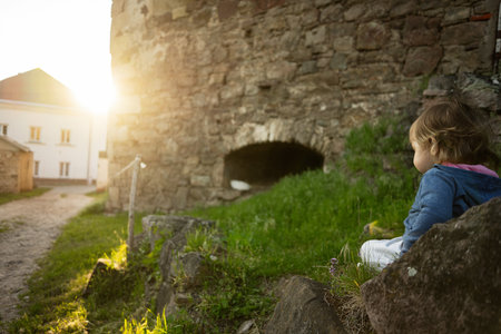 A serene scene of a child sitting near a rustic stone building outdoors.の写真素材