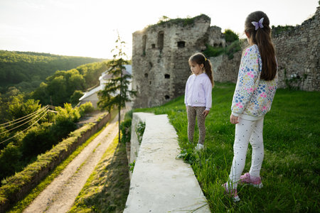 Two young girls observe the scenic countryside near ancient ruins during sunset.の写真素材