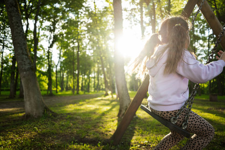 A child swinging outdoors in a serene park surrounded by tall treesの写真素材