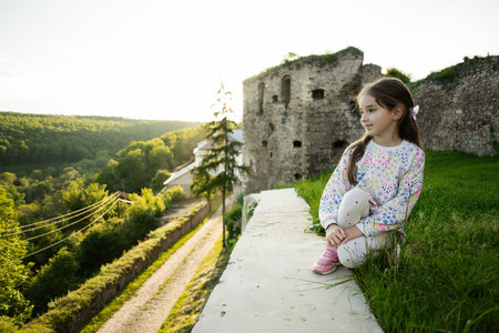 A little girl sits near ancient ruins amidst lush green nature.の写真素材