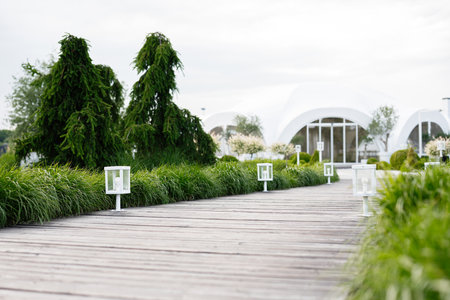 A wooden pathway bordered by grass and lights leading to a futuristic white domeの写真素材
