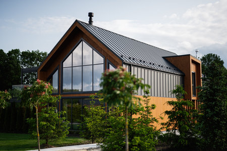 Contemporary residence with wooden siding, metal roof, large windows, and lush green surroundings.の写真素材