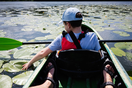 A young boy kayaking on a tranquil lily-covered lake during a bright sunny day