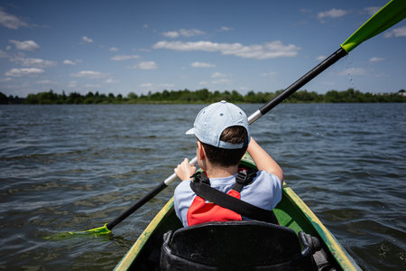 A boy paddling a kayak on a serene lake, enjoying the summer outdoorsの写真素材