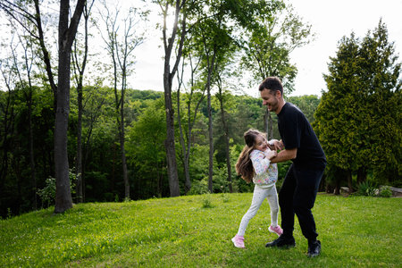 A father and daughter share a fun moment in a beautiful forested park settingの写真素材