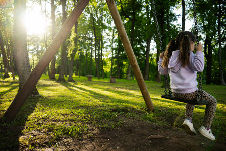A child enjoys a swing in a forest park as sunlight filters through trees.の写真素材
