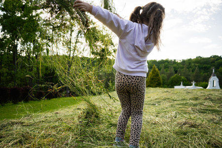 Young girl enjoying the outdoors surrounded by greenery while tossing grass in sunlight