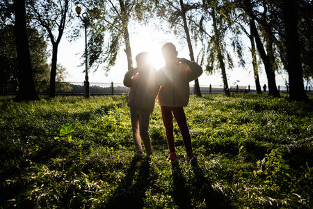 Two children enjoy playing in the park under sunlight and tree canopiesの写真素材