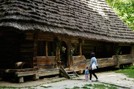 A woman and her daughter walking near a traditional wooden house with thatched roof.の写真素材