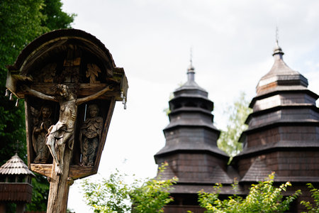 A detailed wooden crucifix with a traditional church in a serene natural settingの写真素材