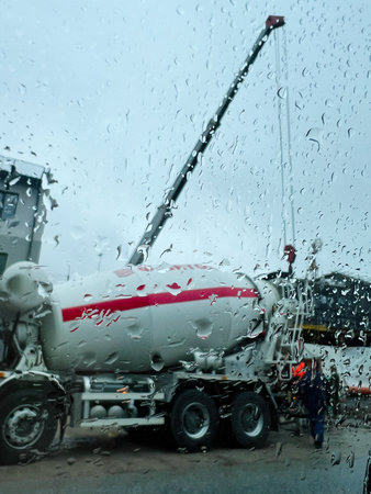 Rainy day at a construction site with truck and crane, seen through raindropsの写真素材