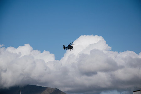 A helicopter soaring in a blue sky over clouds and mountain in Akranes, Iceland.