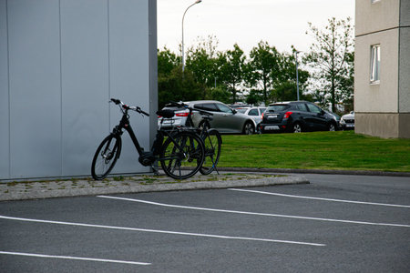 Two bicycles parked beside a building with a parking lot and grassy area visible.