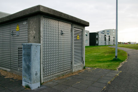 Steel-clad electricity structure near grass and residential buildings in a serene Icelandic...