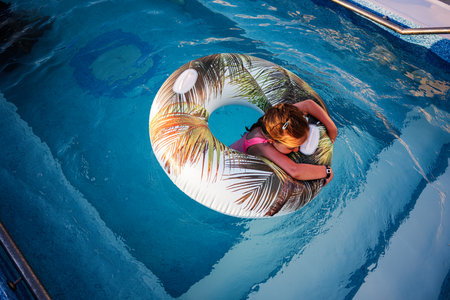 Child relaxing on float in sunny swimming pool with tropical design