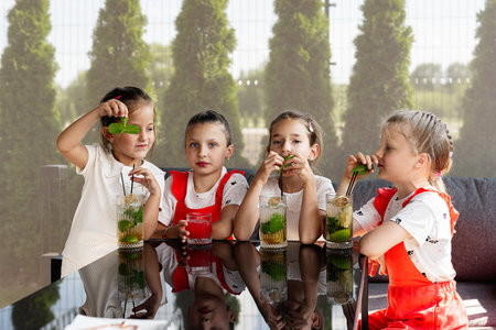 Children seated outdoors drinking refreshing beverages, enjoying the sunny day together.の写真素材