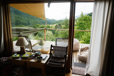 Cozy wooden interior with deck showcasing lush landscape and relaxing outdoor seatingの写真素材
