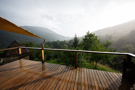 A serene view of a wooden terrace over a rainy, misty forest landscape.