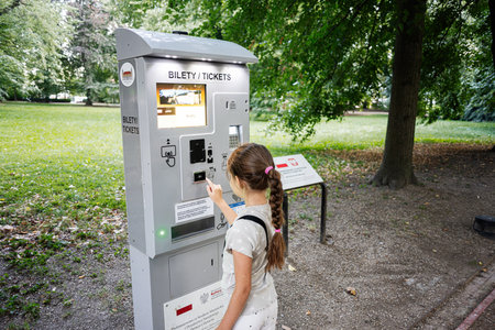 Young girl operates a ticket machine surrounded by nature in Lancut, Poland