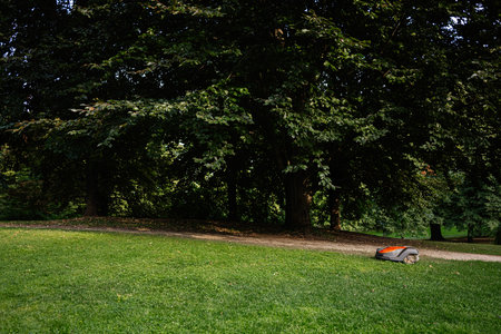 A robotic lawnmower operating on vibrant grass surrounded by trees in tranquil Lancut, Polandの写真素材