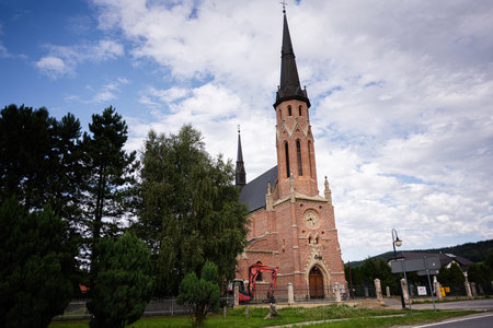 A Gothic-style red brick church of St. Joseph surrounded by greenery in a serene setting in...
