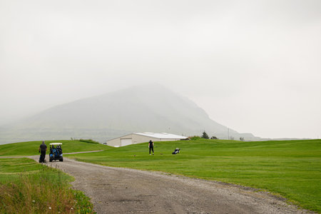 Golfers enjoying a scenic course in Iceland surrounded by misty mountains and greenery.の写真素材