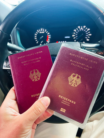 German passports held by hand in a vehicle interior with a steering wheel viewの写真素材