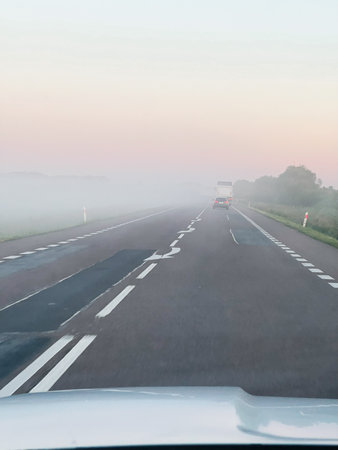A misty highway under gentle pink sunrise tones, portraying tranquility and early morning charm.の写真素材