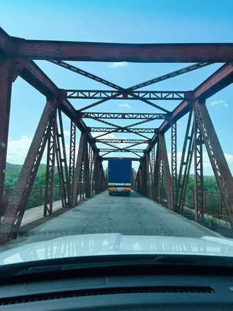 Truck passing on a narrow iron bridge under clear blue sky with vegetation aroundの写真素材