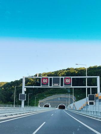 Highway view featuring a tunnel entrance, road signs, and a clear blue skyの写真素材