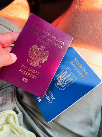 Two Poland and Ukraine passports being held in a hand shown outdoors in natural sunlight.の写真素材