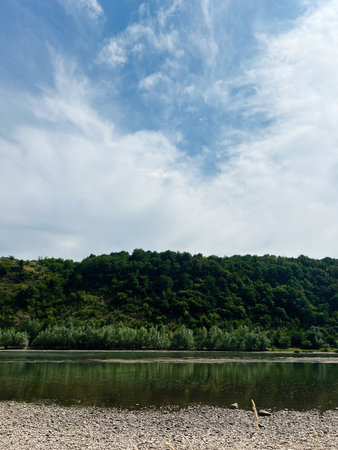 Tranquil nature view featuring a calm river, green trees, and a vibrant sky