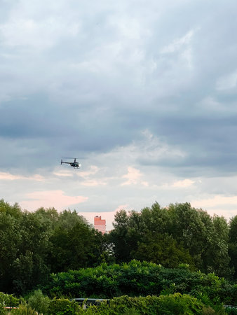A helicopter hovers above a forested area under a cloudy colorful evening sky.の写真素材
