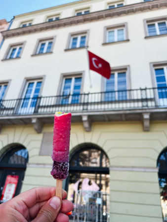 A hand holds pink ice cream in front of Turkish flag on a historic buildingの写真素材
