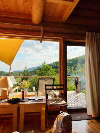 A cozy wooden interior with an inviting terrace view of greenery and hills.の写真素材