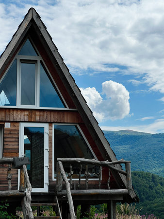 Charming wooden A-frame cabin surrounded by lush mountains under a clear blue sky.の写真素材