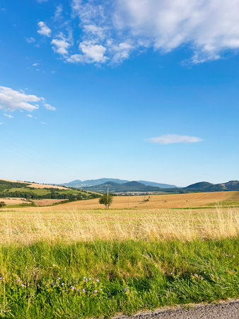 Rolling countryside hills with green grass, blue skies, and distant mountains.の写真素材