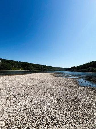 Pebbled river scenery with vivid blue sky and surrounding green landscape.の写真素材