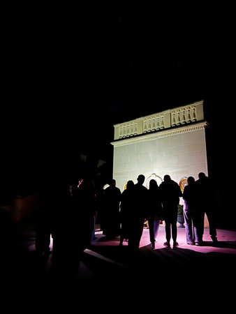 Silhouettes of prayers individuals against a lit structure under a dark starry night skyの写真素材