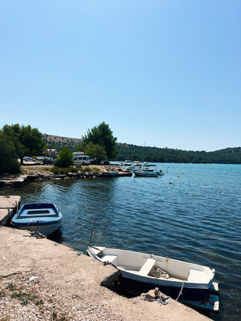 Peaceful seaside scene with boats docked, surrounded by trees and hills in Jadrtovac,Croatia.の写真素材