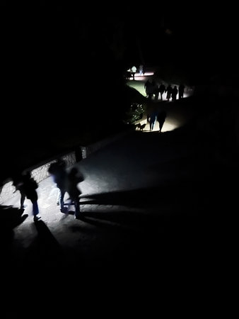 Silhouettes of individuals walking along a dimly lit path during the nightの写真素材