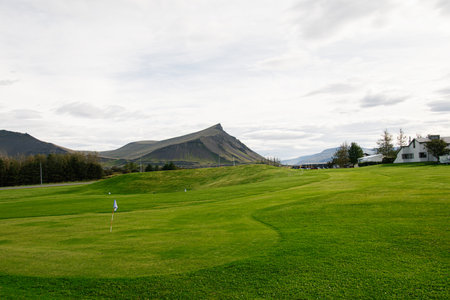 Green golf course nestled amidst scenic mountains and natural Icelandic beautyの写真素材
